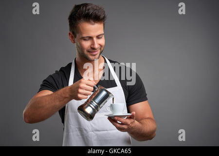 Ein junger Barista Mann lächelnd und gießen Kaffee aus einer Kaffeemaschine, einem coffeecup Stockfoto