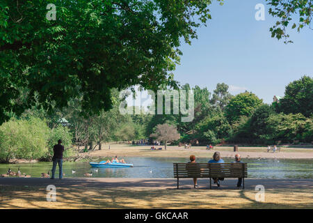 Regent's Park in London, Aussicht an einem Sommernachmittag von Touristen auf einer Bank sitzend beobachten Menschen auf dem See zum Bootfahren, Großbritannien. Stockfoto