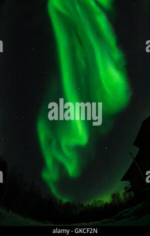 Eine grüne Aurora wirbelt über das Dach eines Hauses. Stockfoto