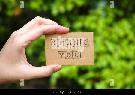 Frau Hand mit Pappkarte mit Worten danke von schwarzen Alphabet Stempel gegenüber grünen Blumen Hintergrund gemacht. Stockfoto