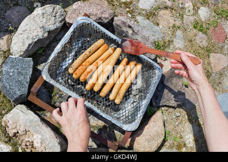 Prozess der echten Braten Schweinswürstl auf einem chinesischen Einweg-Kohle-Grill. Hände kippen Fleisch einen hölzernen Rechen. Ansicht von oben. Sonnigen s Stockfoto