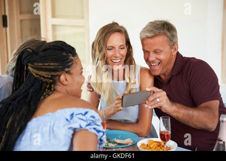 Freunden an einem Tisch schauen Sie sich Bilder auf einem smartphone Stockfoto