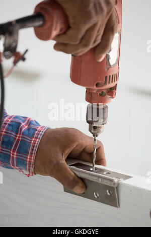 Tür-Montage. Arbeiter bohrt ein Loch für die Schraube des Scharniers Stockfoto