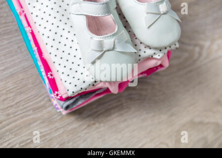 Gefaltete rosa und Weiße Strampler mit Schuhen auf grau Holz- Hintergrund. Windel für neugeborene Mädchen. Stapel kleinkind Kleidung.ch Stockfoto