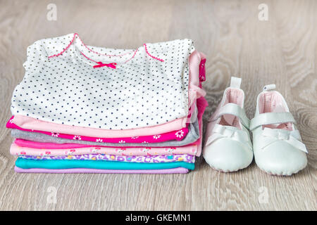 Gefaltete rosa und Weiße Strampler mit Schuhen auf grau Holz- Hintergrund. Windel für neugeborene Mädchen. Stapel kleinkind Kleidung.ch Stockfoto