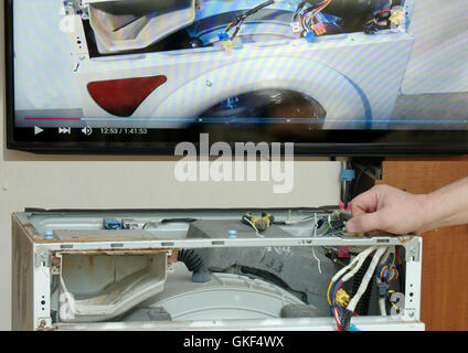 Mechaniker ist eine Waschmaschine zu reparieren, verwenden die video-Anleitungen auf dem TV, reparieren ihre eigenen Hände Stockfoto