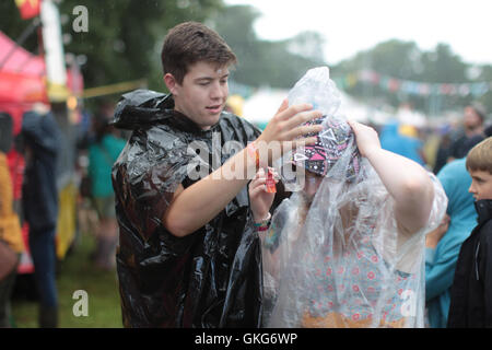 Brecon Beacons, Wales, UK. 19. August 2016. Ein Mann hilft einen Freund in einen Poncho Grüner Mann Festival 2016 in den Brecon Beacons in South Wales Credit: Roger Garfield/Alamy Live News Stockfoto