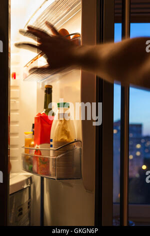 Hand geht für Lebensmittel im Kühlschrank zu Hause abends Stockfoto