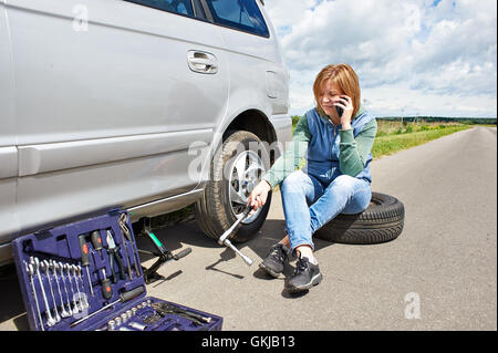 Frau mit Telefon ruft im Dienst der Reservereifen sein Auto Stockfoto