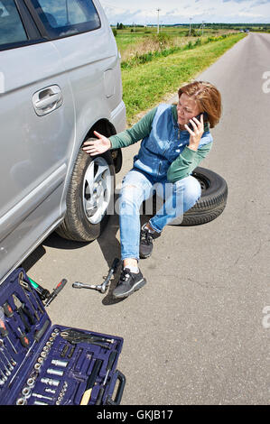 Frau mit Telefon ruft im Dienst der Reservereifen sein Auto Stockfoto