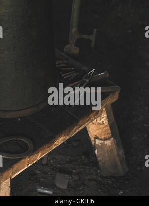 Eine Reihe von alten Schmied-Tools auf einem Holztisch mit einem Eimer. Innerhalb einer traditionellen gälischen Schmiedewerkstatt. Stockfoto