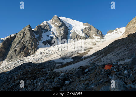 Orange Zelt unter den Steinen in Highland Camp gegen Berge und Gletscher Stockfoto