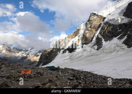 Orange Zelt unter den Steinen in Highland Camp gegen Berge und Gletscher Stockfoto