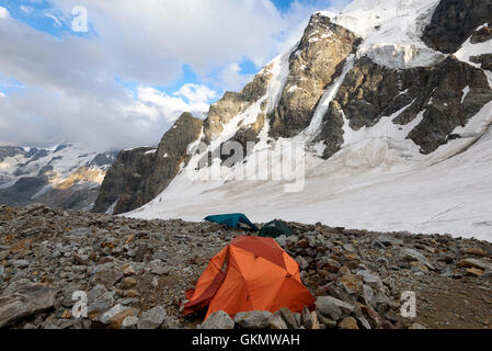 Orange Zelt unter den Steinen in Highland Camp gegen Berge und Gletscher Stockfoto