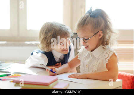 Zwei kleine Klassenkamerad, Laddie und girlie, am gleichen Schreibtisch sitzen. Niedliche Schulmädchen mit Brille schreibt etwas. Die neighb Stockfoto