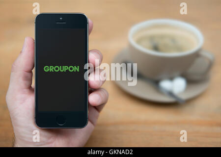 Ein Mann schaut auf seinem iPhone zeigt die Groupon logo, während sie Sitzen mit einer Tasse Kaffee (nur redaktionelle Nutzung). Stockfoto