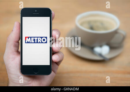 Ein Mann schaut auf seinem iPhone die Metro-Logo anzeigt, während bei einer Tasse Kaffee (nur zur redaktionellen Verwendung) saß. Stockfoto