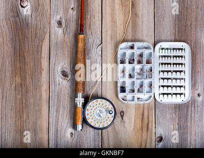 Draufsicht der antiken Fliegenrute, Rolle und Kunstköder Container mit fliegen auf urigen Holzbrettern. Stockfoto