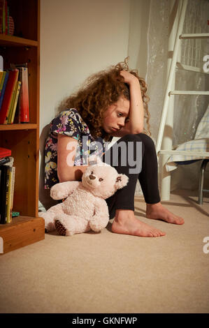 Kind verärgert und allein sitzen auf dem Boden neben einem Bücherregal in ihrem Schlafzimmer. Stockfoto