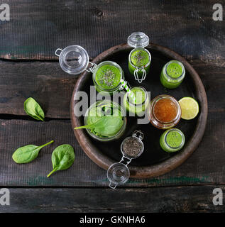 Geöffnete Gläser und eine Flasche grün Spinat Smoothie, serviert mit Baby-Blattspinat, Chiasamen, Honig und Kalk im dunklen Ton Stockfoto