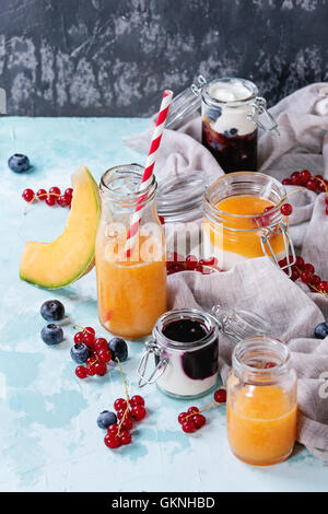 Vielzahl von Melone und Heidelbeeren Smoothie in Gläser und eine Flasche mit Joghurt und rote Johannisbeere Berry, serviert auf leichte blaue textu Stockfoto