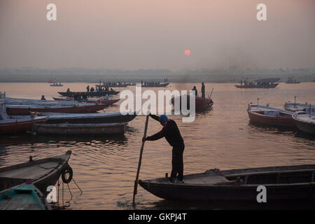 Ein Fährmann navigiert seinen Holzboot beim Sonnenaufgang über dem Ganges in Varanasi, Indien. Stockfoto