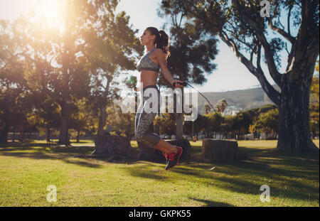 In voller Länge Portrait von Fit junge Frau mit einem Springseil im Park an einem Sommertag überspringen. Stockfoto