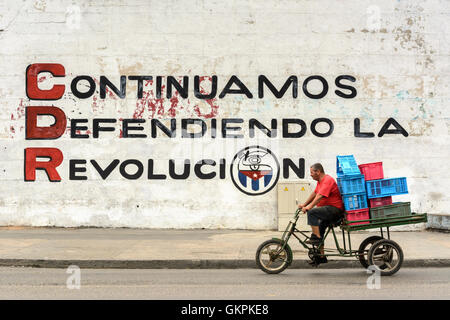 Eine kubanische Mann Zyklen vorbei an einem revolutionären Wandbild in Havanna, Kuba Stockfoto