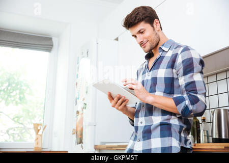 Attraktive junge Mann im karierten Hemd stehend und mit Tablet auf die Küche Stockfoto