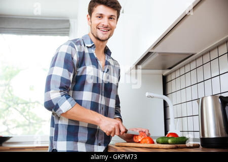 Fröhliche junger Mann im karierten Hemd Schneiden von Gemüse für Salat auf die Küche Stockfoto