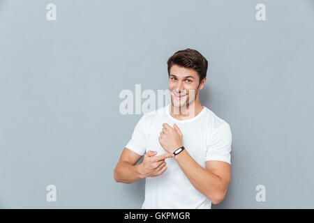 Fröhlichen jungen Mann stehen und deutete auf Fitness-Tracker auf grauem Hintergrund Stockfoto