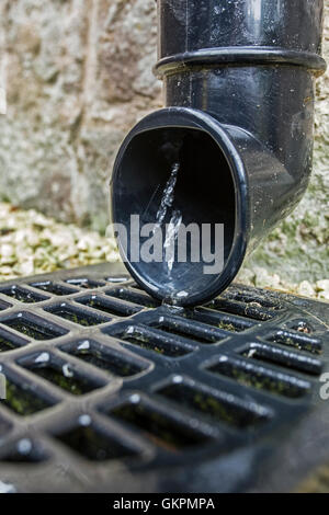 Wasser fließt aus einer Dachrinne Fallrohr in einen Gully. Stockfoto