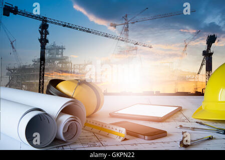 Schreibtisch von Dipl.-Ing., mit Bauplan und Sicherheitsausrüstung gegen Hochbau arbeiten. Stockfoto
