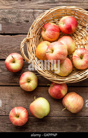 frische rote Äpfel im Weidenkorb auf Holztisch Stockfoto