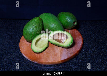 Frische Avocado auf Schneidebrett auf schwarzem Hintergrund Stockfoto
