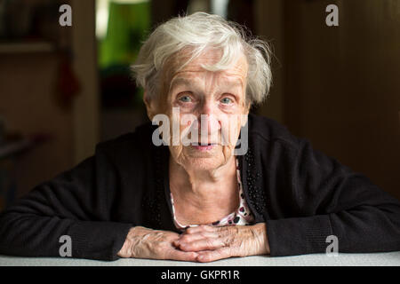 Eine ältere Frau, eine Rentnerin, Closeup Portrait in einem dunklen Raum. Stockfoto