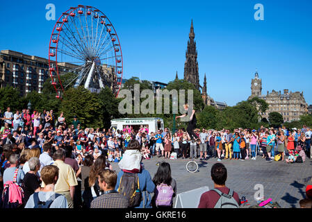 A Street Performer unterhält das Publikum auf The Mound während des Edinburgh Fringe Festivals mit Riesenrad, Scott Monument Stockfoto