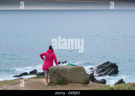 Eine Frau trägt einen bunten Mantel mit Blick aufs Meer auf der Landspitze in Newquay, Cornwall zu. Stockfoto