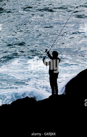 Die Silhouette eines Mannes Angeln vom Felsen in Newquay, Cornwall. Stockfoto