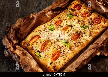 Frisch gebackene traditionelle italienische Focaccia mit Tomaten auf einem alten Holztisch. Stockfoto