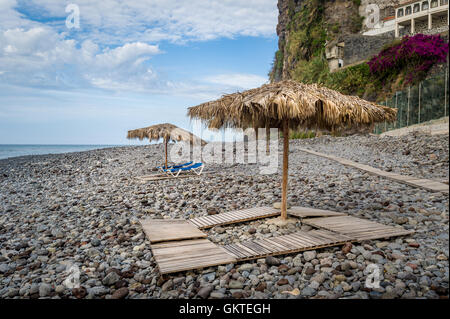 Strohgedeckte Sonnenschirme und Holzbetten in Ponta do Sol, die Insel Madeira. Stockfoto