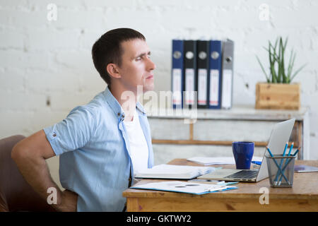 Jung betonte Geschäftsmann vor Laptop sitzt und hält seine Taille mit gequälten Ausdruck. Business Mann Schmerzen Stockfoto