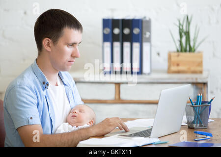 Seite Ansicht Porträt von Ernst lässig junger Vater hält seinen schlafenden neugeborenen Baby während der Arbeit am Laptop im home-office Stockfoto