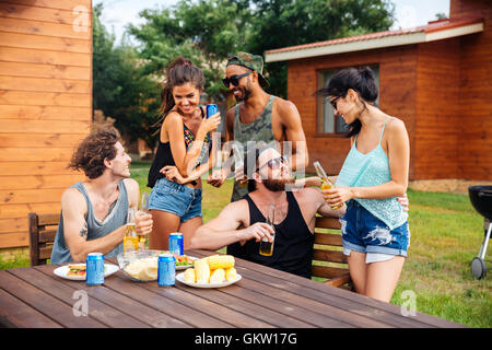 Glückliche Gruppe befreundeter Teenager sitzen am Tisch, trinken Bier und Snacks zu essen Stockfoto