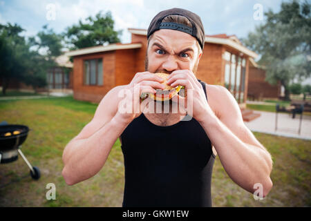 Junge bärtige Hipster Kerl beißen leckere Burger im freien Stockfoto