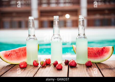 Konzept Foto Alkoholflaschen mit frischen Erdbeeren und Hälften der Wassermelone mit Pool auf dem Hintergrund Stockfoto