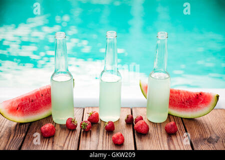 Konzept Foto Alkoholflaschen mit frischen Erdbeeren und Hälften der Wassermelone mit Pool auf dem Hintergrund Stockfoto