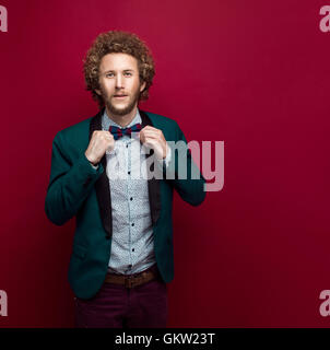 Bärtige stilvollen Mann mit lockigem Haar, Fliege, grüne Jacke tragen. Roten Hintergrund. Isoliert Stockfoto