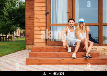 Glückliches junges Paar sitzt und auf der Veranda des Hauses umarmt Stockfoto