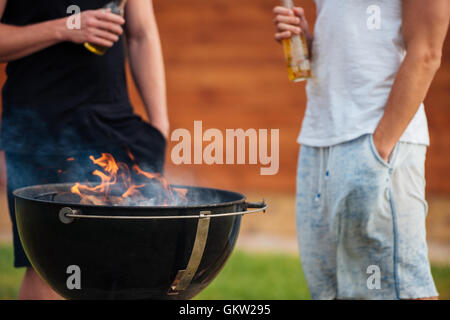 Zugeschnittenes Bild von zwei Männern hält eine Bierflasche während der Vorbereitung der Barbecue-Grill in Parkzone Stockfoto